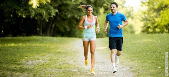 Ein Mann und eine Frau beim Joggen im Wald – doch ist Sport bei Halsschmerzen sinnvoll?