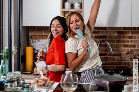 Zwei Freundinnen singen beim gemeinsamen Kochen in der Küche