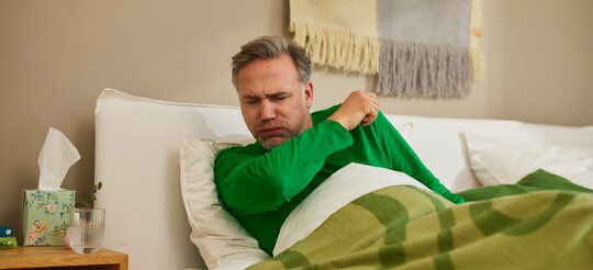 Kranker Mann liegt im Bett mit Husten und Heiserkeit-Symptomen. Mann liegt im Bett hustet aufgrund von Heiserkeit oder Reizhusten.