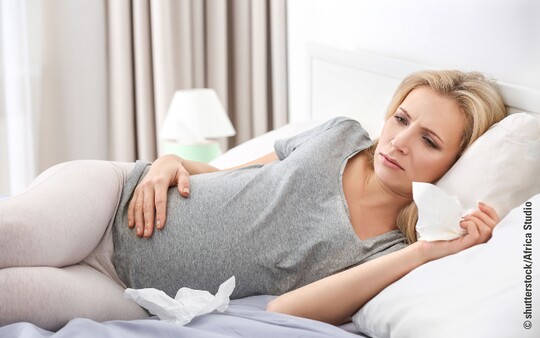 Eine schwangere Frau liegt im Bett und leidet an Reizhusten