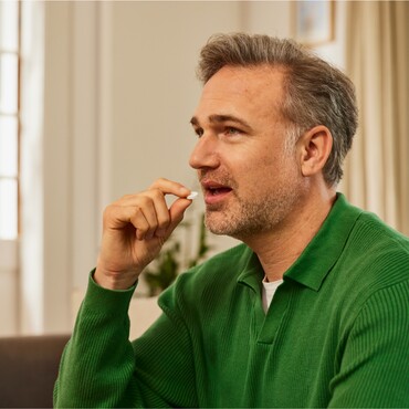 Mann in grünem Pullover nimmt eine GeloRevoice® Halstablette zur Linderung von Heiserkeit.