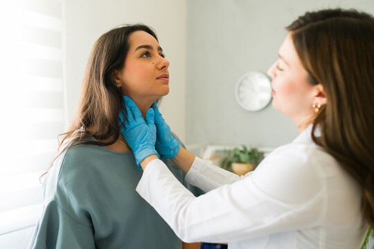 Eine Ärztin tastet mit Handschuhen den Hals einer Patientin ab.